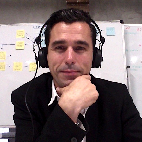 Davido, English Language Coach in Hong Kong. He's wearing black Sennheiser hd-25 headphones, a black jacket over a white shirt and sits in front of a whiteboard